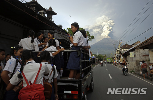 【발리=AP/뉴시스】인도네시아 발리섬 여학생들이 28일 트럭을 타고 등교하고 있다. 그 뒤로 아궁 화산에서 연기와 화산재가 치솟고 있는 모습이 보인다. 2018.11.28