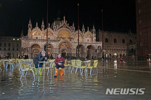 이탈리아 베네치아 성 마르코 광장에 12일(현지시간) 바닷 물이 들어차 관광객 두 명이 장화를 신은 채 의자에 앉아 있다. (출처: 뉴시스)