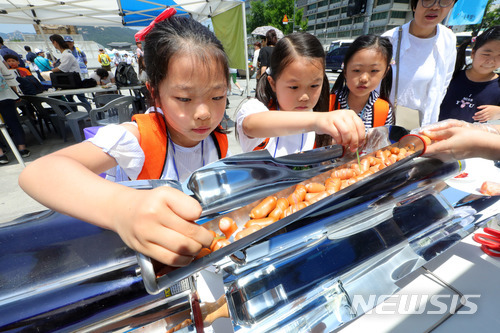 【서울=뉴시스】 16일 오후 서울 종로구 광화문광장에서 열린 2018 에너지수호천사단 나눔장터에서 아이들이 태양열로 구운 소시지를 먹고 있다.