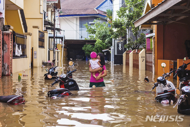 지난 1월 23일(현지시간) 인도네시아 남술라웨시 마카사르에 홍수가 나 한 여성이 자신의 아이를 안고 대피하고 있다. 이번 폭우로 댐이 넘치고 산사태가 발생해 최소 6명이 숨지고 2000명 이상의 이재민이 발생했다고 현지 관계자가 밝혔다. (출처: 뉴시스)