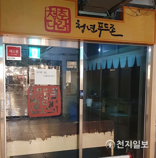 [천지일보 진주=최혜인 기자] 줄폐업으로 불 꺼진 청춘다락 출입문 유리창에 새로 개장한 ‘비단길’의 환한 불빛이 비친다.  ⓒ천지일보 2019.1.18