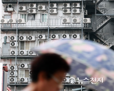 장마전선의 영향으로 폭염 속 습도가 높아져 후텁지근한 날씨를 보인 18일 오후 양산을 쓴 한 시민이 서울 남대문로에 에어컨 실외기로 가득 찬 외벽 앞을 지나가고 있다. ⓒ천지일보
