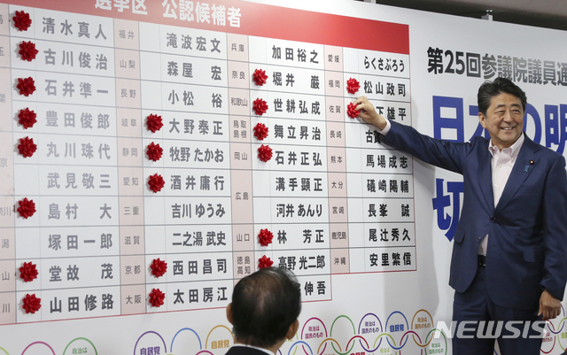 아베 신조 일본 총리가 21일 일본 도쿄 자민당 선거상황실에서 참의원 선거에서 승리한 여당 후보 당선자의 이름 옆에 당선 축하 표시 장식을 달고 있다. (출처: 뉴시스)