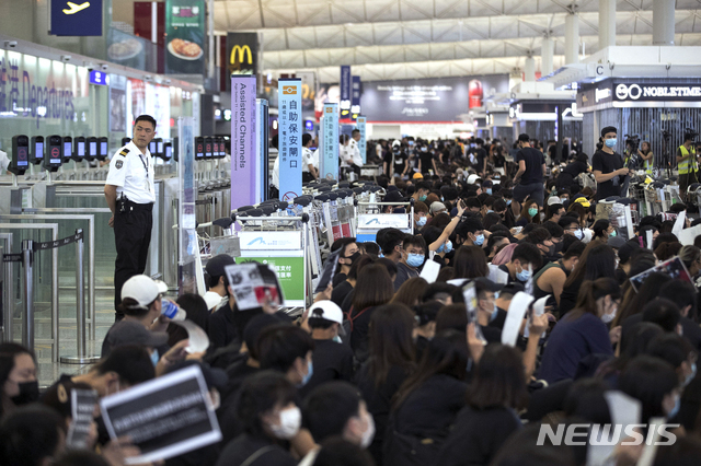 홍콩 국제공항에서 13일 2층 출국 홀을 점거한 시위대가 수하물 카트를 몰고와 출국 게이트 앞을 봉쇄한 가운데 한 공항 보안요원이 게이트 앞에서 뒷짐 지고 이를 보고 있다. (출처: 뉴시스)