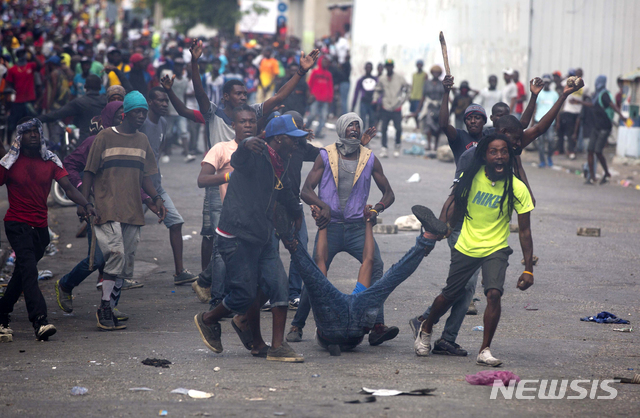 12일(현지시간) 아이티 수도 포르토프랭스 대통령궁 인근에서 조베넬 모이즈 대통령의 퇴진을 요구하는 반정부 시위가 열려 시위대가 경찰이 발사한 총에 맞아 숨진 한 남성의 시신을 끌고 경찰을 향하며 시위를 이어가고 있다. (출처: 뉴시스)
