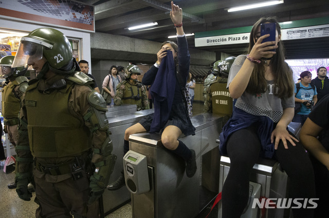18일(현지시간) 칠레 산티아고의 한 지하철역에서 학생들이 회전식 개찰구를 막고 지하철과 버스 요금 인상에 항의하는 시위를 벌이는 중에 칠레 경찰이 주변에서 대응하고 있다(출처: 뉴시스)