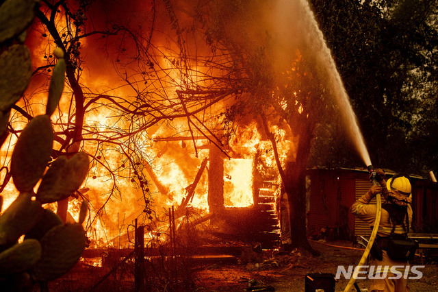 미 캘리포니아주 소노마 카운티에 '킨케이드 파이어(Kincade Fire)'로 이름 붙인 대형 산불로 24일(현지시간) 불붙은 한 주택에 한 소방관이 물을 뿌리고 있다(출처: 뉴시스)