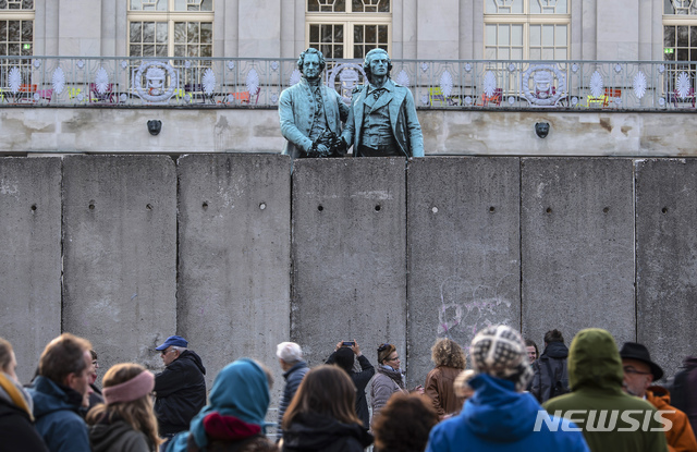 독일 바이마르의 국립극장에서 베를린 장벽 붕괴 30주년을 앞두고 아트 퍼포먼스 '함께 오르는 벽' 행사가 열려 사람들이 독일 시인 괴테와 실러 동상 앞에 임시로 설치된 벽 앞에 모여 있다. (출처: 뉴시스)