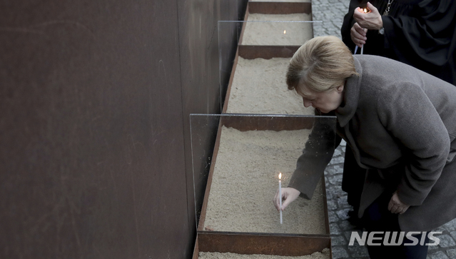 9일(현지시간) 독일 베를린에서 열린 '베를린 장벽 붕괴 30주년' 기념식에서 앙겔라 메르켈 총리가 촛불을 밝히고 있다. 이는 베를린 장벽을 넘어 서베를린으로 탈출하려다 동독 경비병의 총격에 숨진 동독 시민들을 추모하기 위한 것이다. (출처: 뉴시스)
