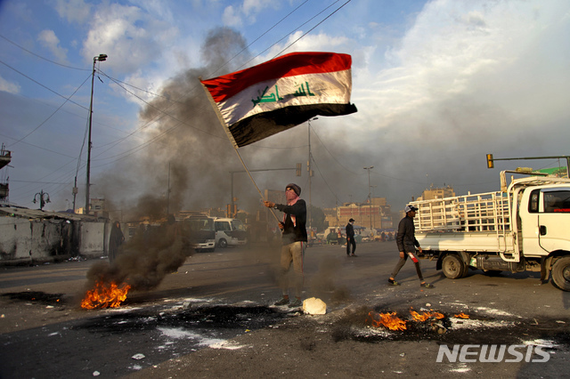 8일(현지시간)  이라크 수도 바그다드의 타흐리르 광장에서 이란의 미군 기지 미사일 공격에 항의하는 시위가 열려 한 남성이 불 타는 도로에서 이라크 국기를 흔들고 있다. 이란은 이날 새벽 솔레이마니 사령관을 사살한 미국의 공습에 대한 보복으로 이라크 내 두 곳의 미군 기지에 미사일 공격을 감행했다. (출처: 뉴시스)