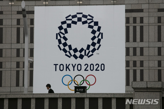지난 23일 도쿄 소재 한 건물에 설치된 2020년 도쿄올림픽 현수막 앞을 시민이 지나가고 있다. (출처: 뉴시스)