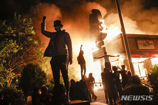 미국 미네소타주 미네아폴리스에서 29일(현지시간) 불타고 있는 식당 앞에서 경찰의 비무장 흑인 남성 살해 사건에 항의하는 시위 참가자들이 주먹을 치켜올려 보이고 있다. (출처: 뉴시스)