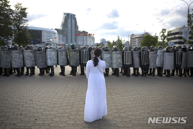 13일(현지시간) 벨라루스 수도 민스크에서 흰옷을 입은 여성 시위자가 보안군 앞에 서있다. 벨라루스에서 지난달 치러진 대선 결과에 불복하는 야권 시위가 한 달 이상 이어지고 있다. (출처: 뉴시스)