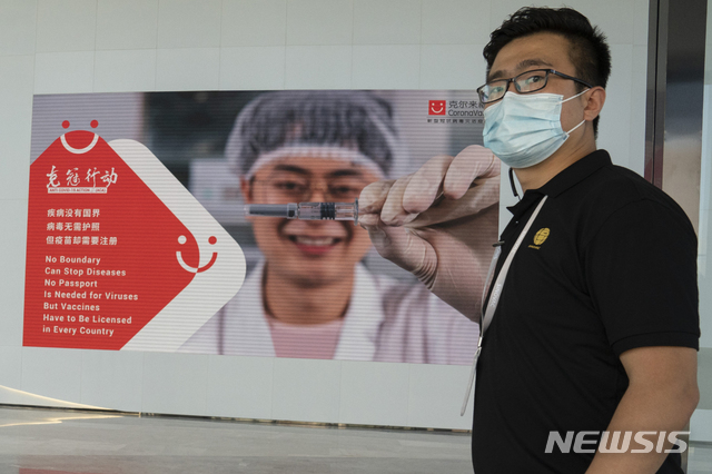 24일(현지시간) 중국 제약사 시노백의 베이징 공장에서 한 직원이 신종 코로나바이러스 감염증(코로나19) 광고판 앞에 서 있다(출처: 뉴시스)