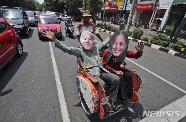 지난 8일 인도네시아 센트라 자바 솔로에서 조 바이든 대통령 당선인과 카멀라 해리스 부통령 당선인의 가면을 쓴 인도네시아 남성들이 대선 결과를 자축하며 세발자전거에 앉아 손을 흔들고 있다. (출처: 뉴시스)