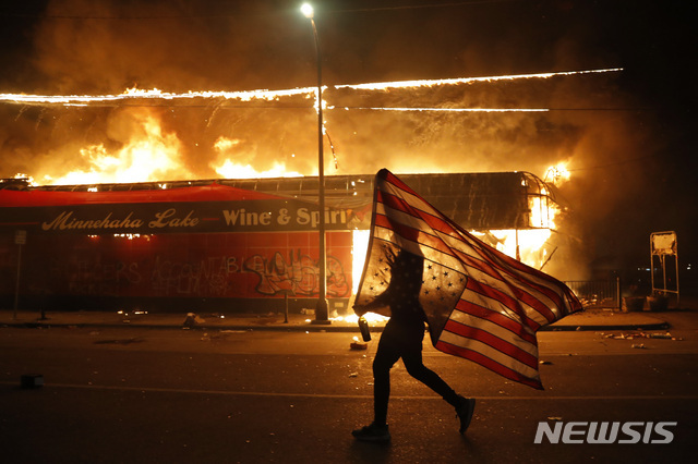 2020년 5월 28일 미국 미네소타주 미니애폴리에서 흑인 남성 조지 플로이드가 경찰의 과잉진압으로 사망한 데 대한 인종차별 항의 시위 도중 한 시위자가 불타는 건물을 지나갈 때 미국 국기를 거꾸로 들고 있다. AP통신은 이 사진을 2020년을 가장 잘 표현한 사진으로 꼽았다. 깃발을 거꾸로 드는 것은 국제적으로 조난 신호다. (출처: 뉴시스/AP)