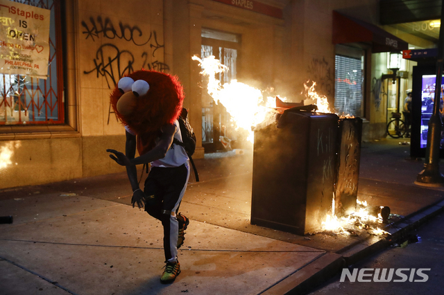 2020년 5월 30일 미국 필라델피아에서 인종차별 항의 시위가 발생한 가운데 엘모 마스크를 쓴 한 시위 참가자가 불 타는 길거리에서 춤을 추고 있다. (출처: 뉴시스/AP)