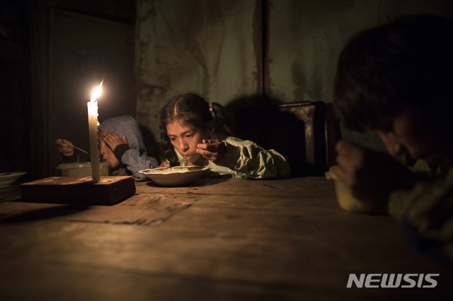 6월 8일 페루 리마에서 에스티엔, 에스테파니, 하비에르 아크노가 전기가 들어오지 않는 누에바 에스페란자 인근의 집에서 촛불을 켜놓고 저녁을 먹고 있다. (출처: 뉴시스/AP)