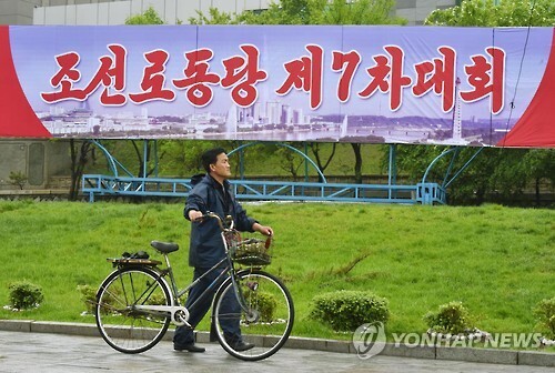 김정은 시대의 선포를 공식화하는 북한의 제7차 노동당 대회가 6일 열렸다. 사진은 대회가 열리는 평양 4·25 문화회관 주변에 설치된 당 대회 알림판 아래를 한 주민이 자전거를 끌고 지나가고 있다. (출처: 연합뉴스)