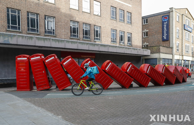 [킹스턴=신화/뉴시스]21일(현지시간) 영국 런던 근교 킹스턴에서 마스크를 쓴 한 남성이 '고장'이라는 제목의 빨간색 전화박스 조각 작품 앞을 자전거로 지나고 있다.