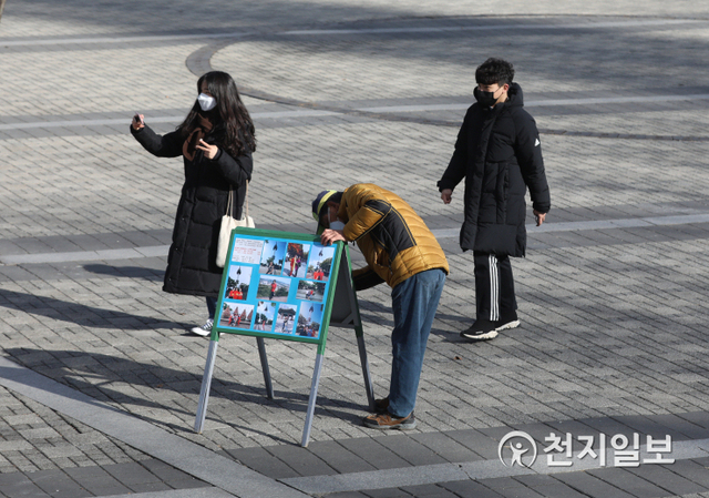 [천지일보=남승우 기자] 자리를 정리하고 있는 사진사 김모씨 뒤로 한 커플이 스마트폰을 들고 사진을 찍고 있다. ⓒ천지일보 2021.2.19