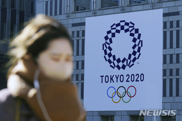 [도쿄=AP/뉴시스]지난 1월 19일 코로나19 예방을 위해 마스크를 쓴 한 여성이 일본 도쿄에서 2020 도쿄 올림픽 현수막 근처를 걷고 있다. 2021.03.09.