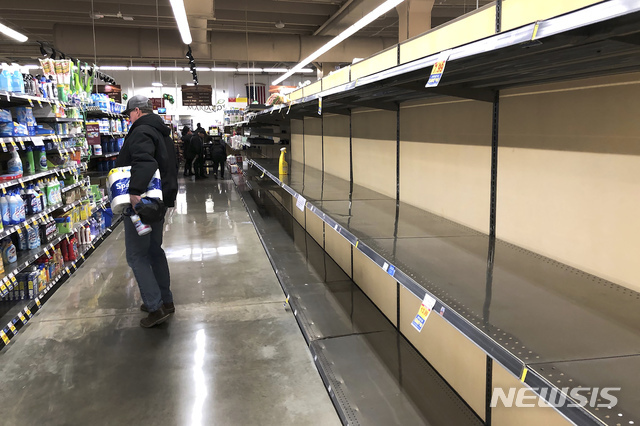 ]미 일리노이주 시카고의 한 슈퍼마켓에서 14일(현지시간) 화장지를 들고 있는 쇼핑객 1명이 텅 빈 식품 진열대 건너편의 청소용품들을 살펴보고 있다. (출처: 뉴시스)