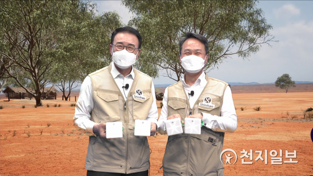15일 조용병 신한금융그룹 회장(왼쪽)과 진옥동 신한은행 은행장이 그룹의 대표적인 사회공헌 프로그램인 ‘2021 글로벌 원 신한 자원봉사 대축제’의 시작을 알리는 ‘태양광 랜턴 만들기’ 행사를 진행하며 신한은행 디지털 방송국에 구축한 AR 스튜디오에서 증강현실을 활용해 구현한 아프리카 마을 현장을 배경으로 직접 만든 태양광 랜턴을 들고 있다. (제공: 신한금융그룹) ⓒ천지일보 2021.6.15