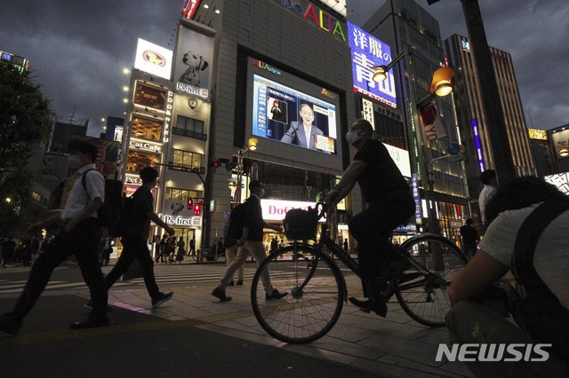 [도쿄=AP/뉴시스] 지난 17일 일본 도쿄의 밤 거리를 마스크를 착용한 시민들이 지나가고 있다. 건물의 대형 스크린에는 스가 요시히데 총리의 기자회견이 생중계되고 있다. 2021.06.22.