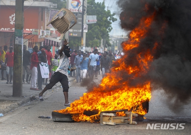 [포르토프랭스=AP/뉴시스]작년 11월 아이티 수도 포르토프랭스에서 베르티에르 전투 제217주년 기념식이 열려 행사 후 조브넬 모이즈 아이티 대통령의 퇴진을 요구하는 시위대 중 한 명이 불타는 장벽에 의자를 던지고 있다.
