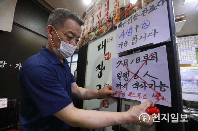 [천지일보=남승우 기자] 수도권에 대한 사회적 거리두기 개편안 시행이 일주일 유예된 가운데 1일 오후 서울 종로구 광화문의 한 음식점에서 사장님이 ‘7월 1일부터 6인까지 식사 가능’이라고 적힌 안내문에 ‘X’ 표시를 하고 있다. 해당 안내문 위에 ‘백신접종 완료자 4명+α 가능합니다’라고 적힌 안내문이 붙어 있다.최근 수도권 위주로 코로나19 신규 환자가 급증함에 따라 정부는 이날부터 예정됐던 새 사회적 거리두기 개편안 시행을 수도권에서만 1주일 유예하기로 했다. 이에 따라 7월 1일부터 7일까지 1주일간은 현행대로 사적모임 5인 이상 금지 등이 동일 적용되고, 이 기간동안 확진자 발생 추이에 따라 8일 이후 새로운 거리두기 적용 여부를 다시 결정하게 된다. ⓒ천지일보 2021.7.1