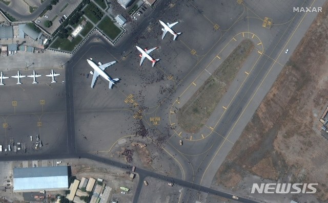 [카불=AP/뉴시스] 지난 16일(현지시간) 공개된 위성 사진에 아프가니스탄 카불의 하미드 카르자이 국제 공항 활주로에 아프간을 탈출하려는 사람들이 항공기에 몰려들고 있다. 2021.08.17.