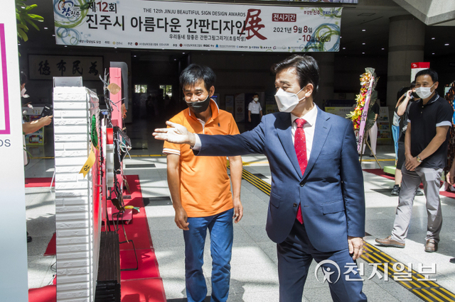 [천지일보 진주=최혜인 기자] 8일 진주시청 로비에서 ‘아름다운 간판 디자인전’ 대상에 선정된 진주실크로 만든 간판이 전시돼 있다. 사진은 기념촬영하는 조규일 진주시장(왼쪽)과 허종우씨.조규일 진주시장은 “독창적이고 세련된 간판은 도시의 품격과 문화 수준을 나타내는 지표가 된다”며 “이번 디자인전을 계기로 광고물의 수준 향상과 바람직한 광고 문화를 한 단계 더 발전시키기를 기대한다”고 말했다.이번 디자인전에서는 창작모형 13점, 창작디자인 39점, 간판 그림 그리기 부문 184점이 응모됐으며 심사위원회의 심사를 거쳐 분야별로 각각 5점, 16점, 23점이 수상작으로 선정됐다.특히 초등학생 공모 부문인 간판 그림 그리기 부문에서는 미래 꿈나무들의 눈높이로 도시 공간을 표현한 작품들이 많이 출품됐다. 디자인전은 오는 10일까지 시청 로비에서 열리며 광고의 역사와 다양하고 독창적인 광고물을 만나볼 수 있다. (사진 제공: 진주시) ⓒ천지일보 2021.9.8