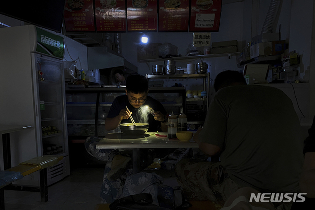 [선양(중국 랴오닝성)=AP/뉴시스]중국 북동부 랴오닝(遼寧)성 선양(瀋陽)의 한 식당에서 29일 한 손님이 정전으로 스마트폰 손전등을 사용해 국수를 먹고 있다. 에너지 절약 목표 달성과 일부 지역에서의 전력 부족 사태 완화를 위한 전력 공급 감축에 따라 중국 북동부 지역에서 29일 사람들은 스마트폰 손전등을 비추어 아침식사를 하고, 상점 주인들은 자가 발전기를 가동시키기 시작했다.