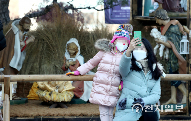 [천지일보=박준성 기자] 25일 서울 중구 명동성당에서 열리는 성탄 미사에 앞서 한 아이와 신자가 성당 앞마당에 설치된 아기예수 말구유 앞에서 사진을 찍고 있다. ⓒ천지일보 2021.12.25