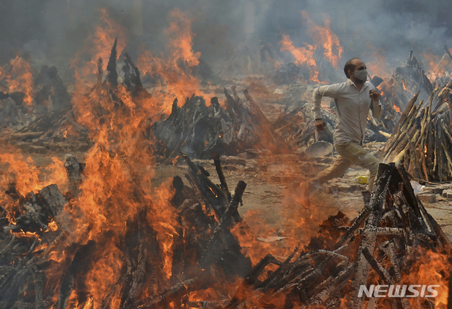 4월 29일 인도 뉴델리 외곽의 화장장에서 한 남성이 코로나19 희생자들의 장작더미에 있던 남성이 더위를 피해 달려가고 있다. 인도에서는 화장 시설이 부족하자 강가에 임시로 시신을 묻는 일도 발생했다. (출처: 뉴시스)