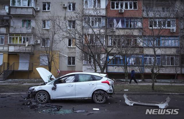 한 남성이 24일(현지시간) 우크라이나 마리우폴에서 러시아의 포격에 파손된 차량과 파편 옆을 지나가고 있다. (출처: 뉴시스)