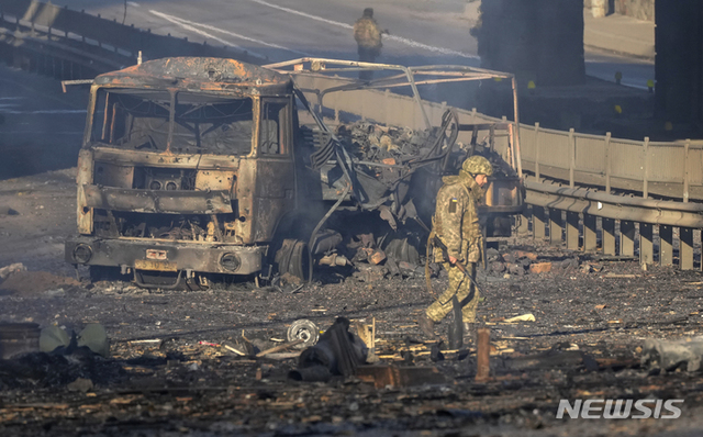 2월 26일(현지시간) 우크라이나 군인이 수도 키예프의 거리에서 불타는 군용 트럭의 잔해를 지나가고 있다. (출처: 뉴시스)