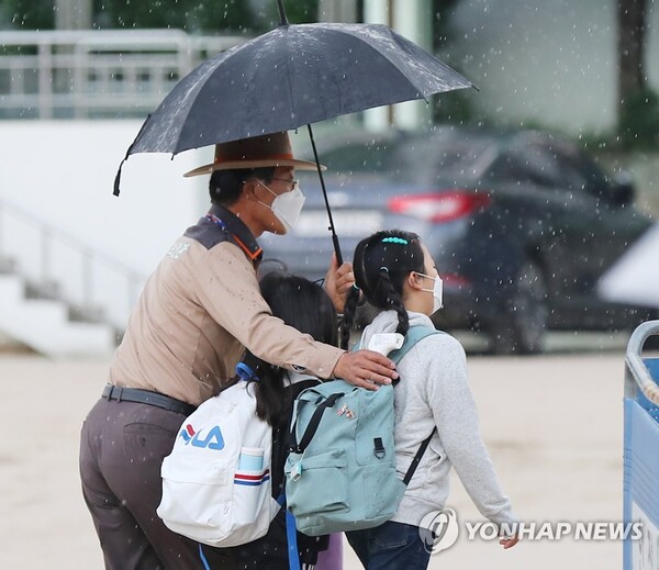 서울 종로구 한 초등학교에서 학교보안관이 우산을 미처 준비하지 못한 아이들에게 우산을 씌워주며 교실로 함께 이동하고 있다. (출처: 연합뉴스)