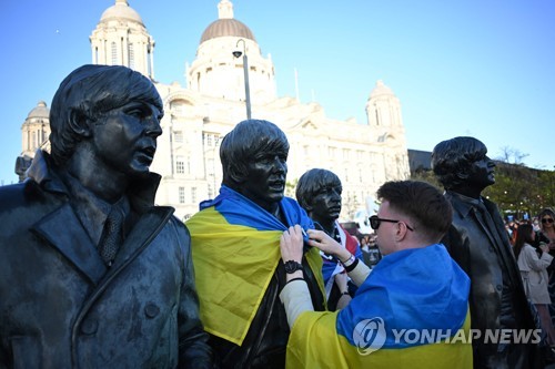 유로비전 결승 전날, 전쟁을 겪고 있는 우크라이나의 한 남성이 조각가 앤디 에드워즈가 만든 비틀즈 동상에 우크라이나 국기를 두르고 있다. (AFP/연합뉴스)