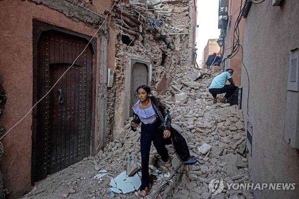 강진이 발생한 모로코 마라케시에서 무너진 건물 사이로 걸어가는 여성. [AFP, 연합뉴스]
