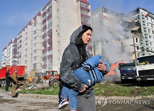 지난달 28일(현지시간) 우크라이나 키이우에서 아이를 안은 한 여성이 러시아 공습으로 파괴된 아파트 건물을 지나가고 있다. 이날 러시아군이 키이우, 드니프로, 폴타바 등 주요 도시를 공격해 최소 8명이 사망했다. (AFP/연합뉴스)