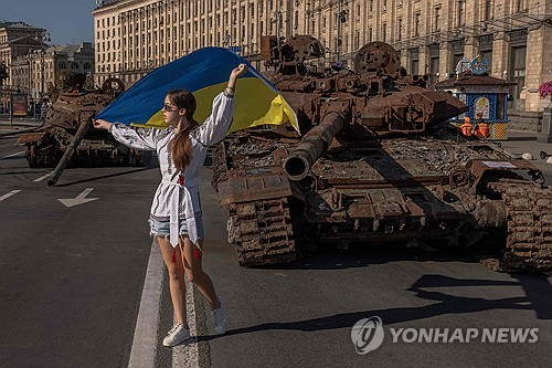 우크라이나 독립기념일인 24일(현지시간) 키이우에서 한 소녀가 파괴된 러시아 장갑차 옆에서 국기를 들고 사진을 찍고 있다. (AFP/연합뉴스) 2023.08.28.