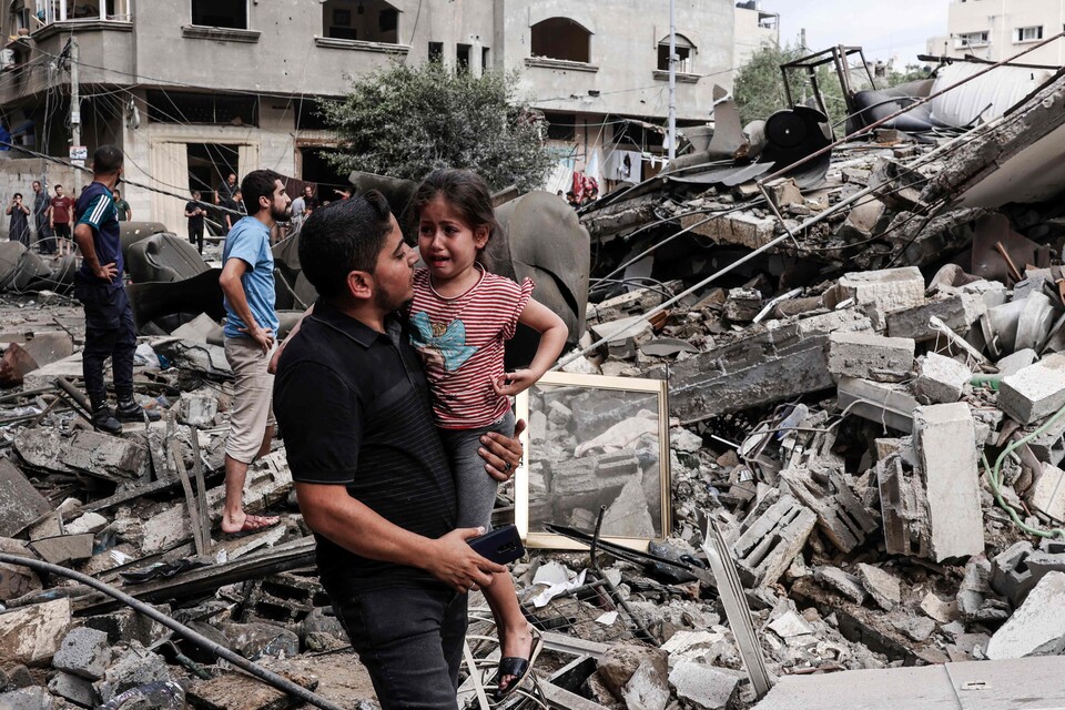 한 팔레스타인 남성이 7일(현지시간) 가자지구에서 이스라엘의 공습으로 파괴된 건물 앞을 걸어가면서 가족을 잃은 한 팔레스타인 아이를 달래고 있다. 2023.10.09.