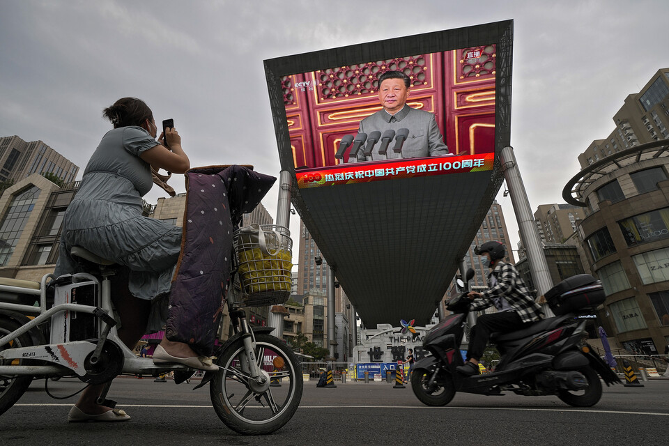 중국 베이징의 톈안먼 광장에서 스쿠터를 탄 한 행인이 대형 비디오 스크린을 통해 연설하는 시진핑 주석의 모습을 찍고 있다. (AP/뉴시스)