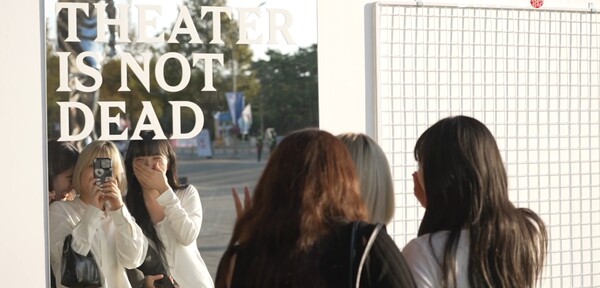 부산국제영화제를 찾은 시민들이 ‘THEATER IS NOT DEAD(극장은 죽지 않았다)’라고 쓰여 있는 포토월 앞에서 사진을 찍고 있다. (출처: 부산국제영화제 공식영상)