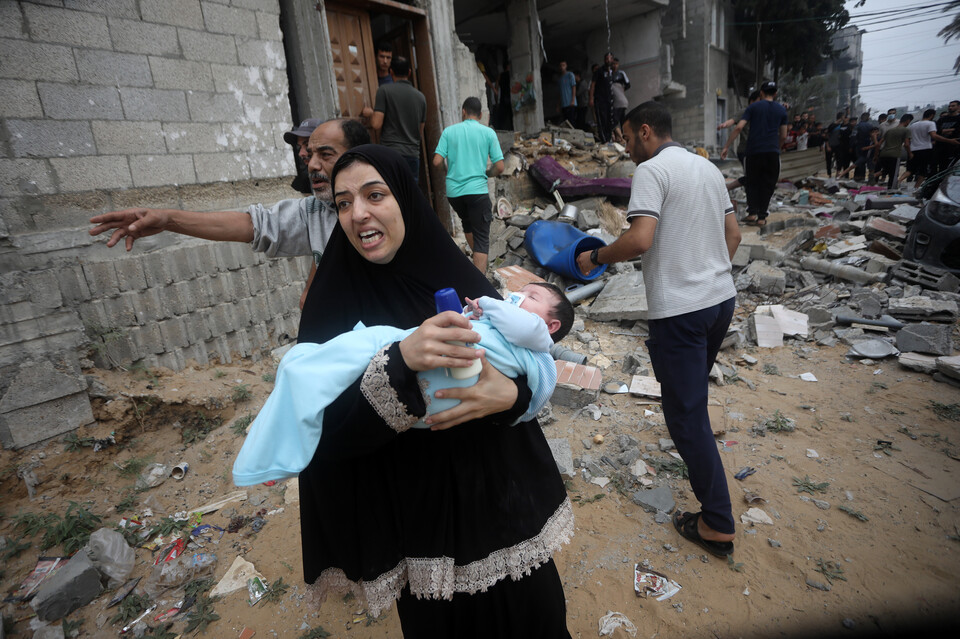한 팔레스타인 여성이 29일(현지시간) 이스라엘군이 폭격을 가한 가자지구 남부 라파 지역에서 아기를 안고 대피하고 있다. (UPI/연합뉴스) 2023.10.30.