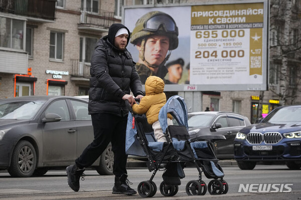 지난 21일(현지시간) 러시아 상트페테르부르크에서 루블로 표시된 급여 금액과 “가입하세요”라는 문구가 적힌 러시아 군대 계약직 홍보 광고판 앞을 아버지와 자녀가 지나가고 있다. (출처: 뉴시스)