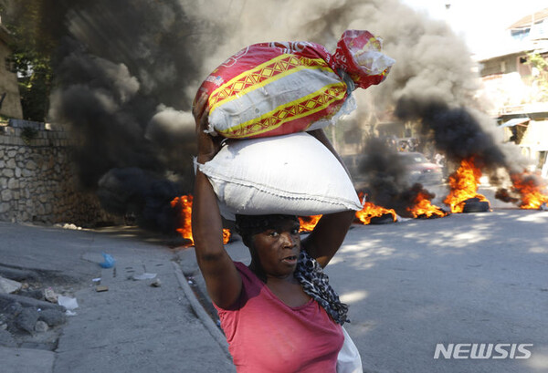 18일(현지시간) 아이티 포르토프랭스에서 총리의 사임을 요구하는 시위가 열린 가운데 한 여성이 불에 탄 타이어를 지나쳐 걸어가고 있다. (출처: 뉴시스)