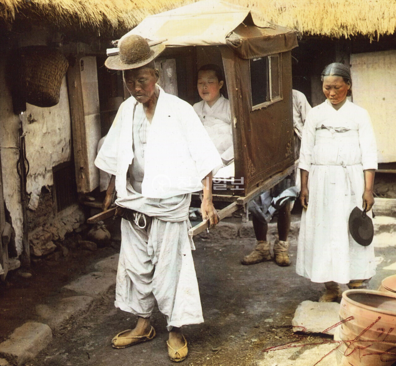 가마 타고 나들이(1903년). 사진 속 가마를 들고 가는 모습을 자세히 보면 앞에 있는 가마꾼(교군꾼)과 뒤에 있는 가마꾼의 모습이 조금 다른 것을 알 수 있다. 대체적으로 뒤에 있는 가마꾼이 더 젊으며, 무엇보다 신발에서도 차이가 난다. 앞선 가마꾼은 맨발에 짚신을 신었다면 뒤에 있는 가마꾼은 덧버선을 필히 신어야 했다. 가마에 시야가 가려져 앞은 물론 가마 아랫부분도 시야 확보가 안 돼 돌부리와 같은 장애물에 발을 다치는 경우가 많기 때문이다. 가마 옆에서 태극선(부채)을 들고 있는 여인은 가마를 타고 있는 몸종으로 보이며 가는 동안 틈틈이 부채로 더위를 식혀주곤 했다. (제공: 정성길 기록사진연구가) ⓒ천지일보 2024.09.16.